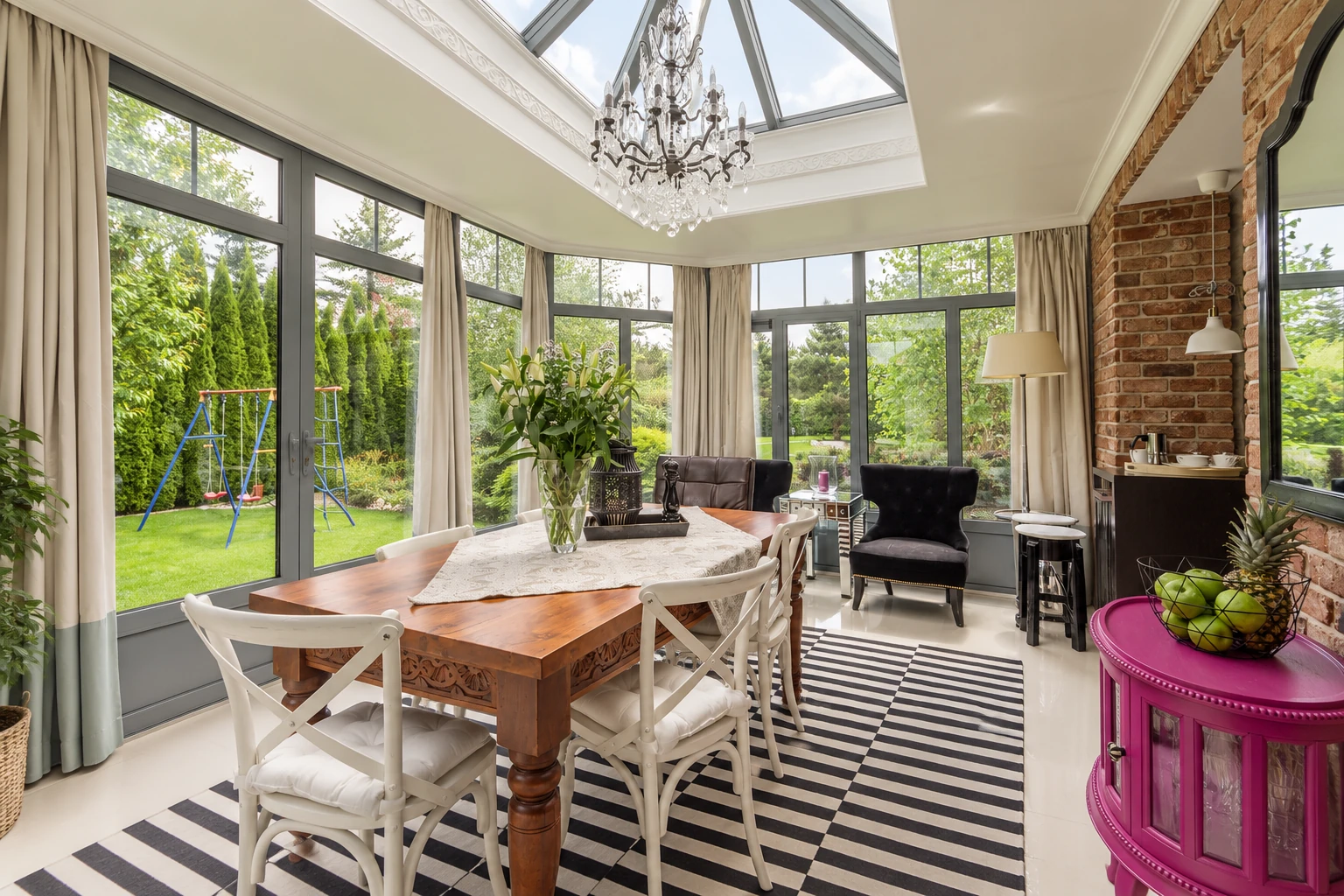 Three-season sunroom with a glass roof, floor-to-ceiling windows, a dining table, and garden views.