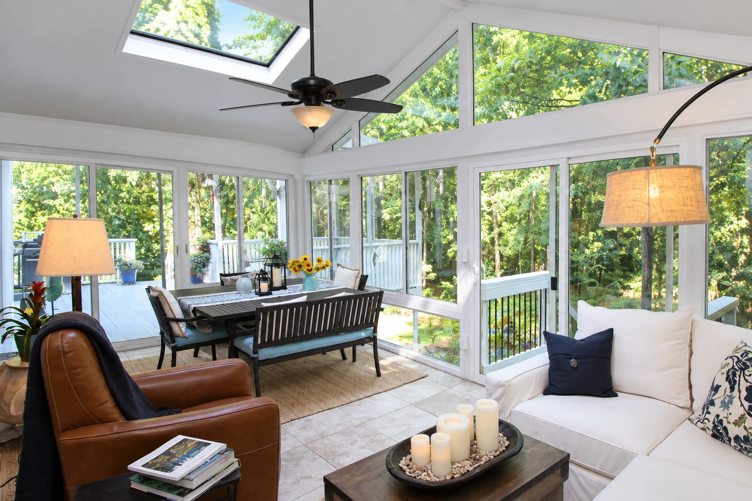 Bright three-season sunroom with white-framed windows, a dining set, ceiling fan, and sofas.